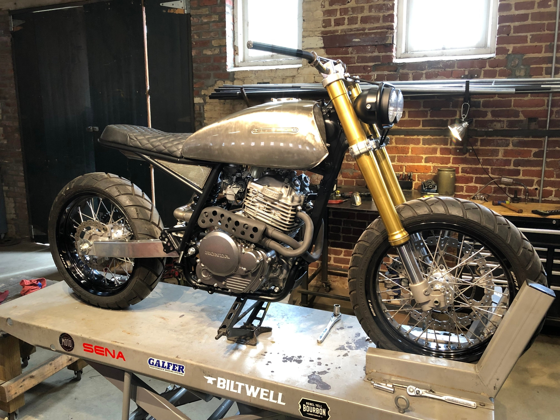 Custom motorcycle on a workshop lift, brick wall behind